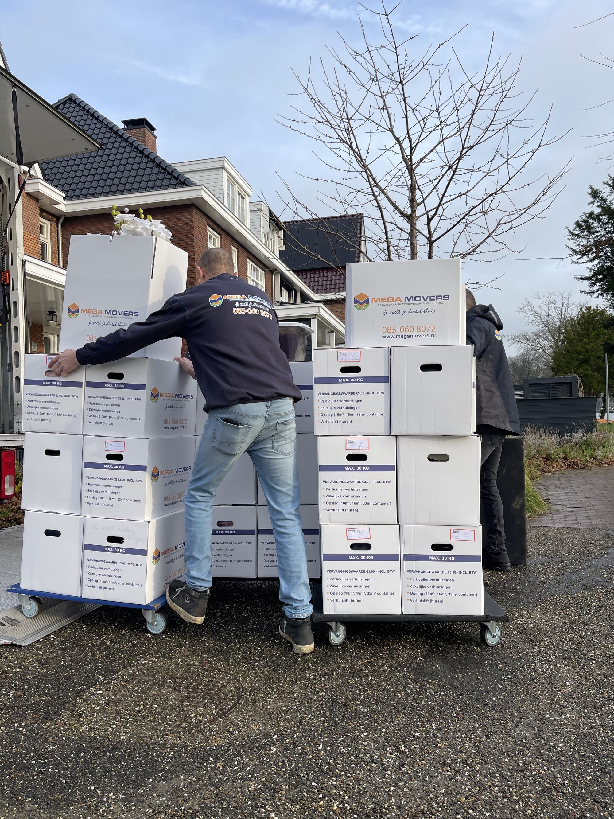 Twee verhuizers stapelen verhuisdozen op de steekwagens
