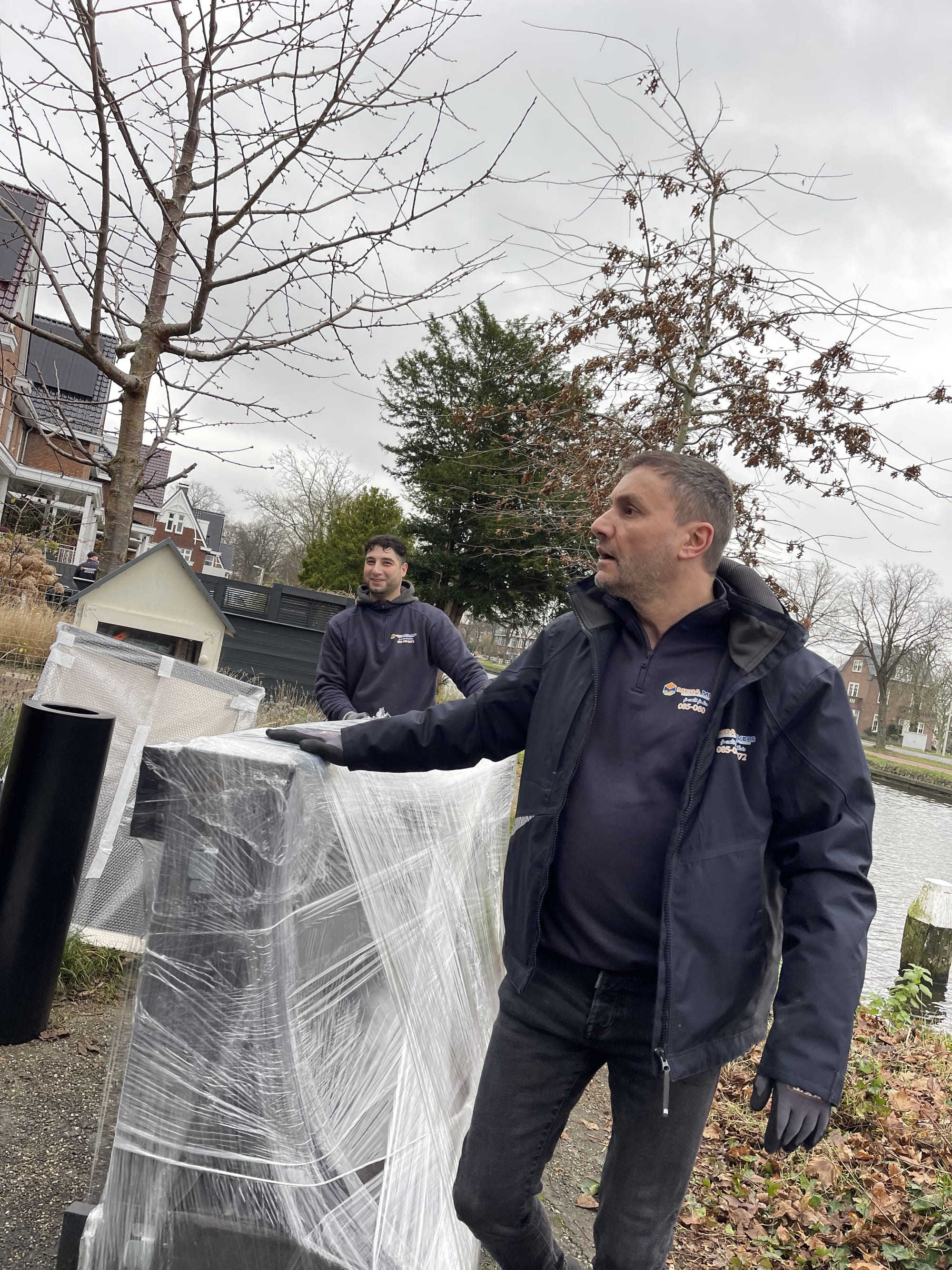 Twee verhuizers met een ingepakt meubel langs de gracht